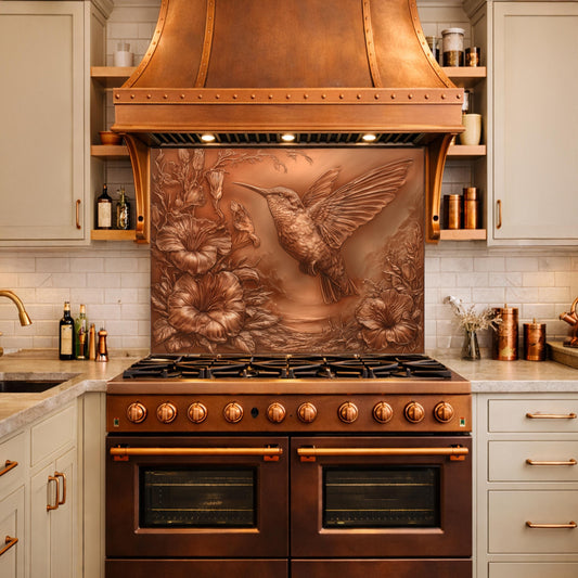May include: A copper range hood with a hummingbird relief above a matching range. The hummingbird is depicted in flight with outstretched wings, surrounded by floral details. The kitchen features light-colored cabinets and a white tile backsplash.
