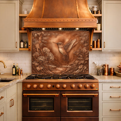 May include: A copper range hood with a hummingbird relief design above a brown oven. The kitchen features light-colored cabinets and a white tile backsplash. The hummingbird is in flight, surrounded by floral and natural elements.